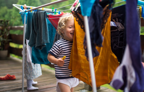 Two happy toddler children standing outdoors on a terrace in summer, playing with clothes drying hanger.