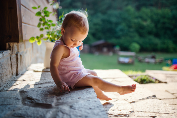 A cute toddler girl sitting outdoors in front of house in summer. Copy space.