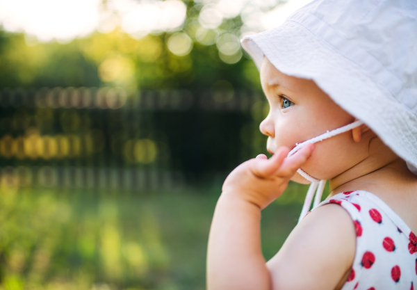 A close-up of toddler girl standing outdoors in garden in summer. Copy space.