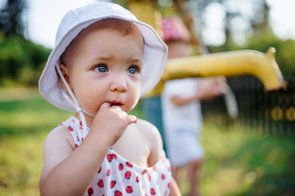 A close-up of toddler girl standing outdoors in garden in summer. Copy space.