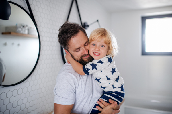 Mature father carrying small son indoors in bathroom, hugging.