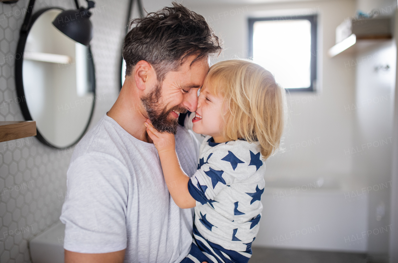 Mature father carrying small son indoors in bathroom, having fun.