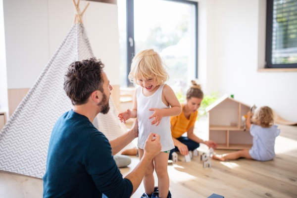 A young family with two small children indoors in bedroom, playing.