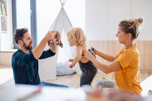 A young family with small child indoors in bedroom getting dressed.