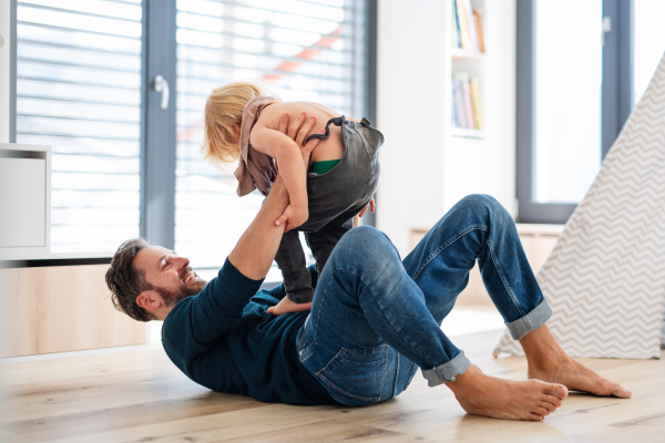 Mature father with small boy playing indoors in bedroom, having fun.