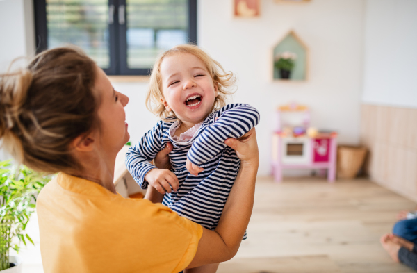 A cheerful young mother with small daughter indoors in bedroom playing.