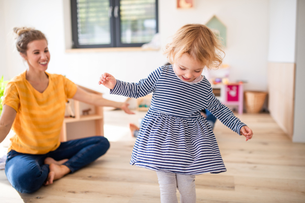 A cheerful young mother with small daughter indoors in bedroom playing.