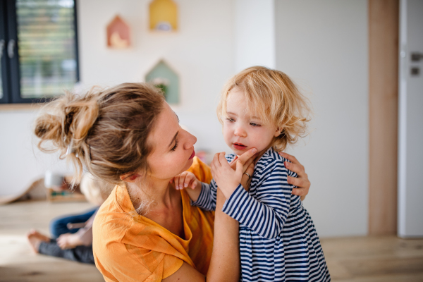 A young mother with small daughter indoors in bedroom talking.