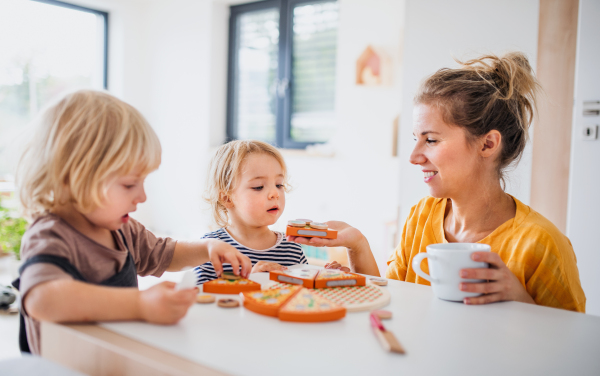 Mother with two small children indoors in bedroom playing with wooden toys.