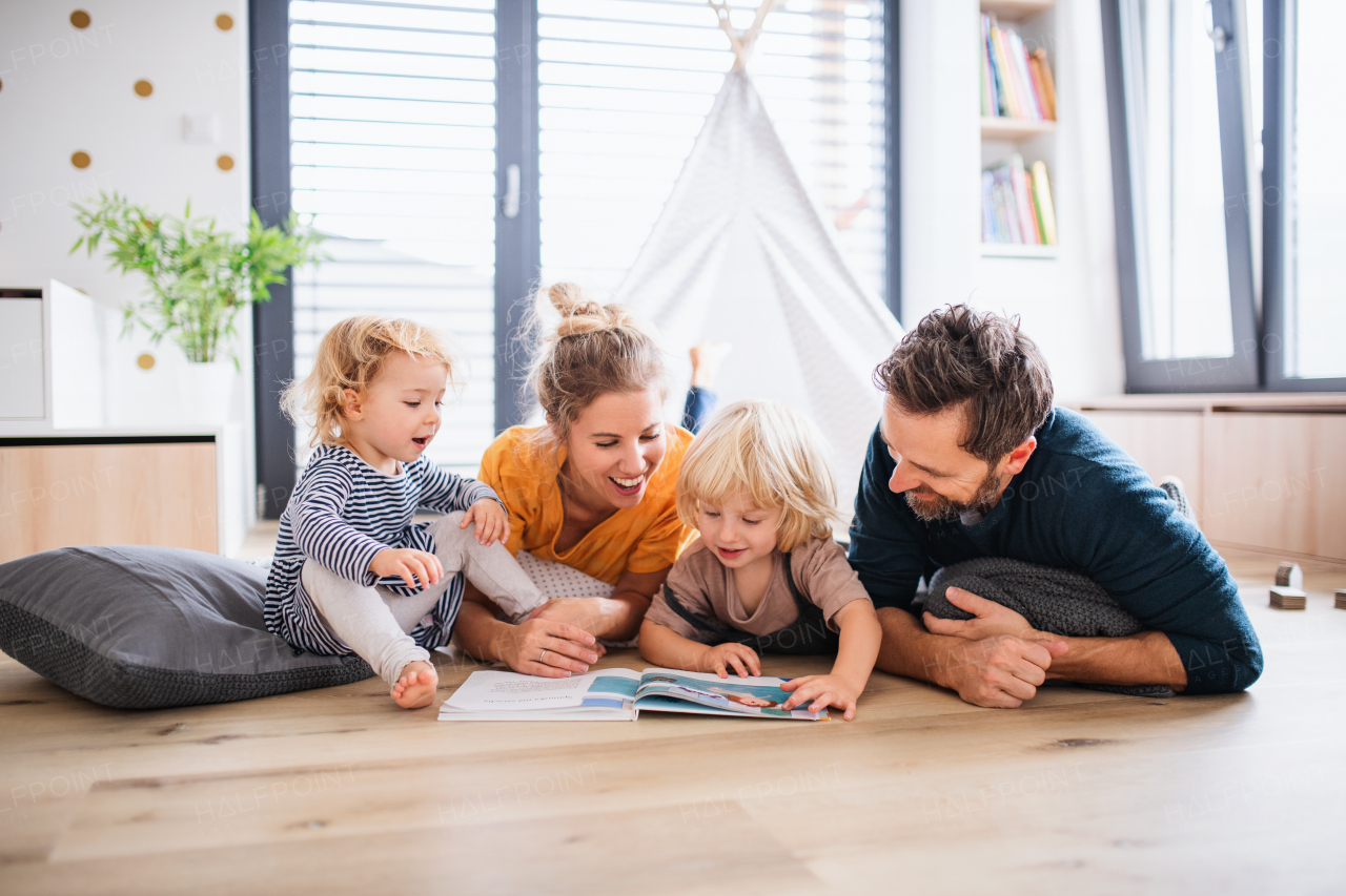 Front view of young family with two small children indoors in bedroom reading a book.