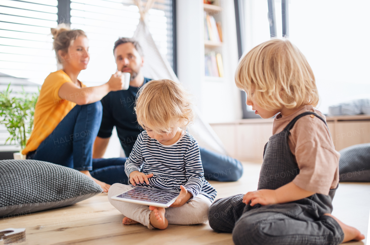 Front view of young family with two small children indoors in bedroom using tablet.