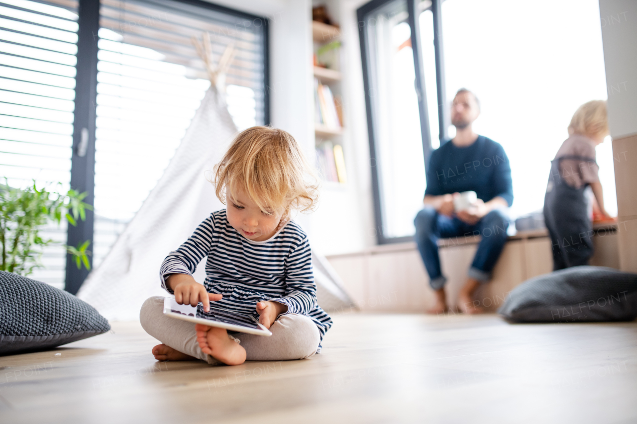 A cute small toddler girl standing indoors in bedroom playing with tablet.