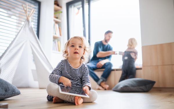 Front view of small toddler girl sitting indoors in bedroom, using tablet.