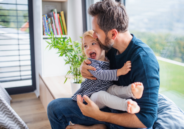 Cheerful young father with small daughter indoors in bedroom playing and hugging.