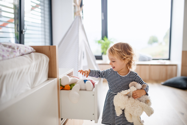 A cute small toddler girl standing indoors in bedroom playing.