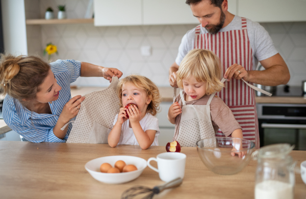 Front view of young family with two small children indoors in kitchen, cooking.