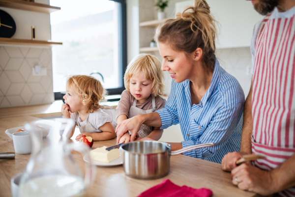 A young family with two small children indoors in kitchen, preparing food.