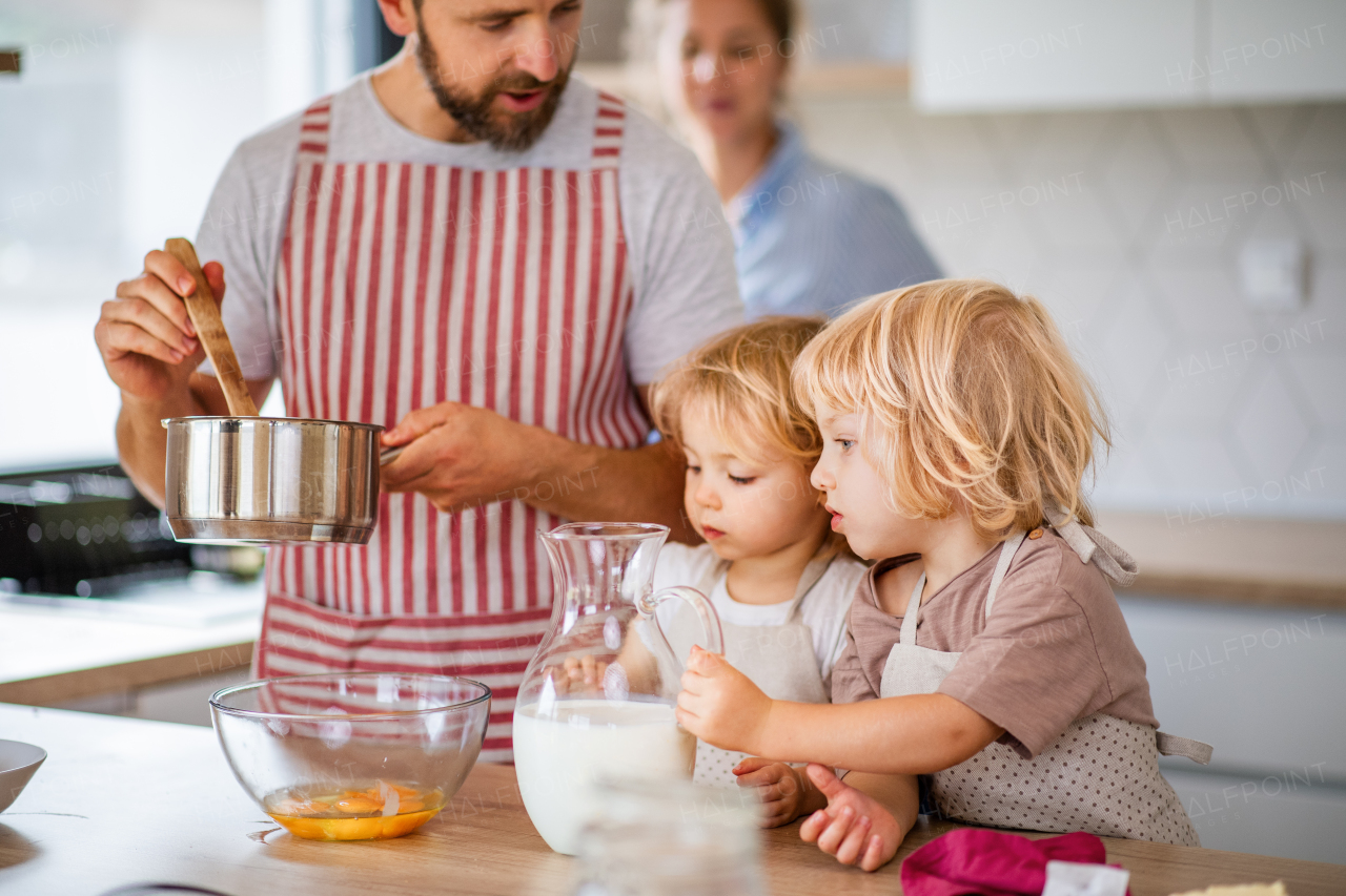 A young family with two small children indoors in kitchen, cooking.