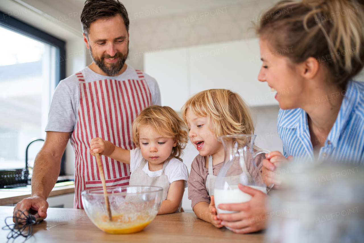 Front view of young family with two small children indoors in kitchen, cooking.