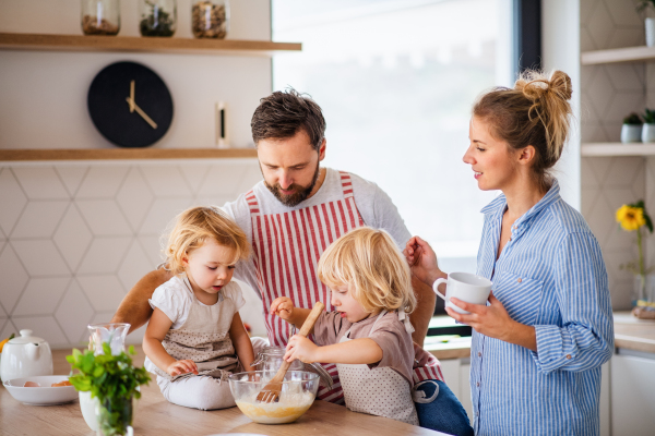 A young family with two small children indoors in kitchen, cooking.