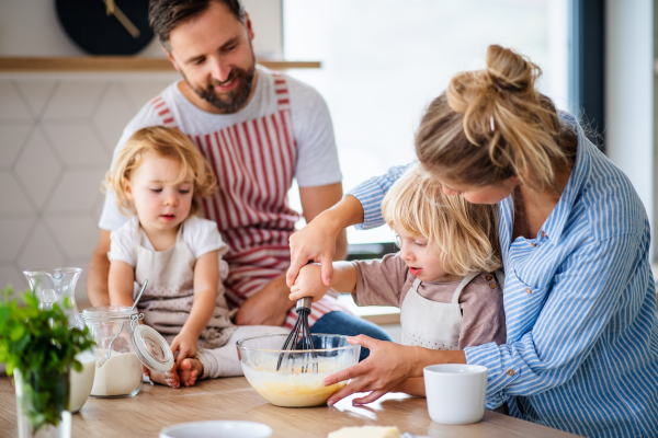 A young family with two small children indoors in kitchen, cooking.