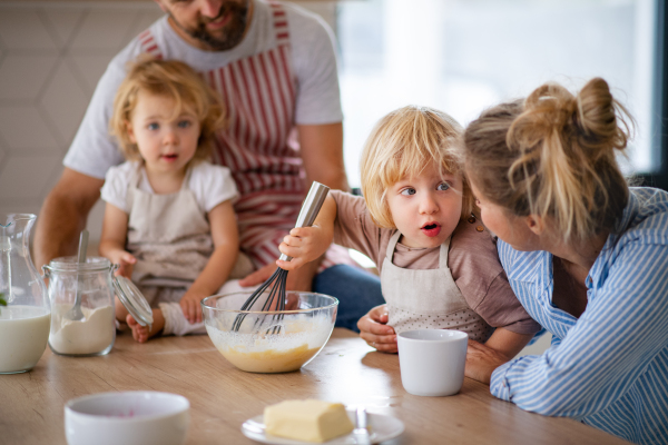 Front view of young family with two small children indoors in kitchen, cooking.