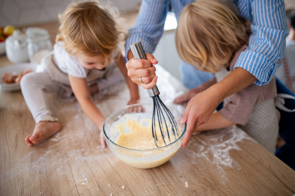 A midsection of mother with two small children indoors in kitchen, cooking.