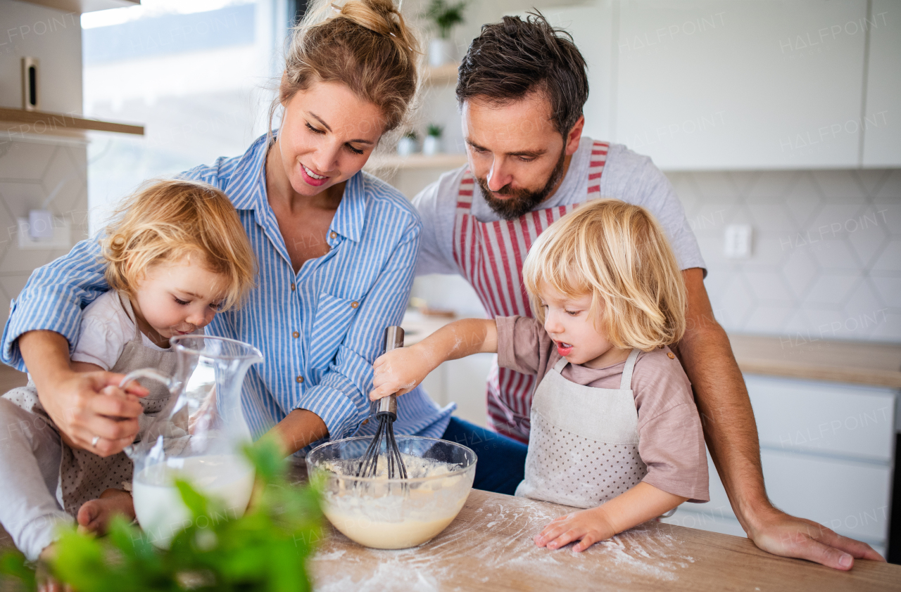 A young family with two small children indoors in kitchen, cooking.