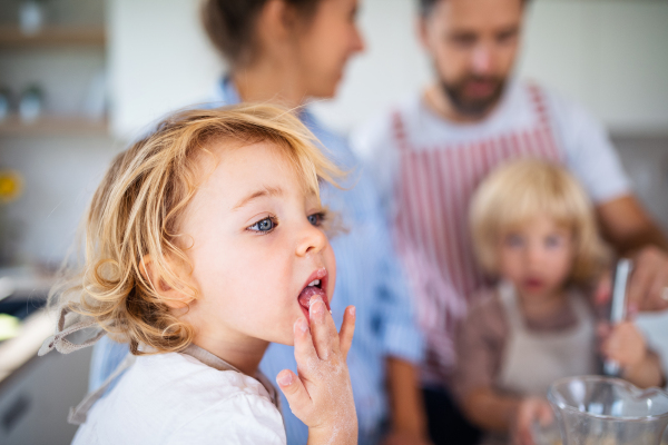 Small girl with family indoors in kitchen, licking fingers when cooking.