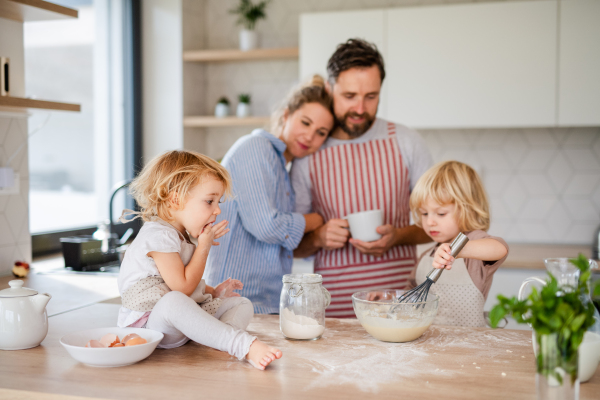 Front view of young family with two small children indoors in kitchen, cooking.