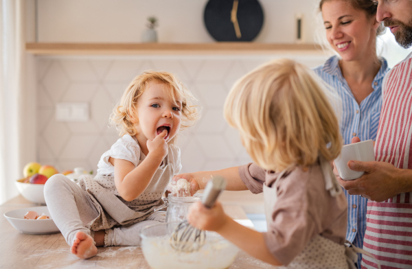 A young family with two small children indoors in kitchen, cooking.