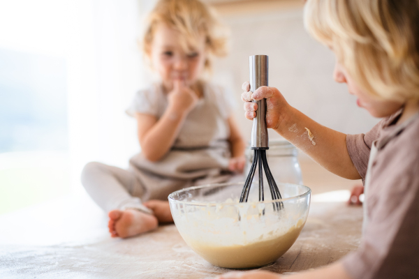 Happy two small children helping indoors in kitchen with cooking.