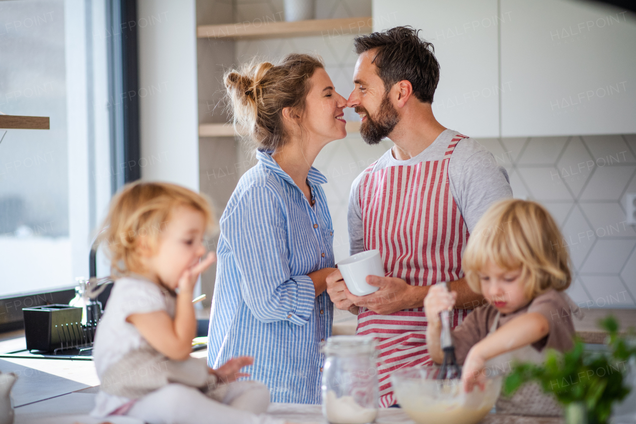 Front view of young family with two small children indoors in kitchen, cooking.