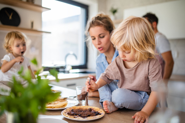 A young family with two small children indoors in kitchen, eating pancakes.