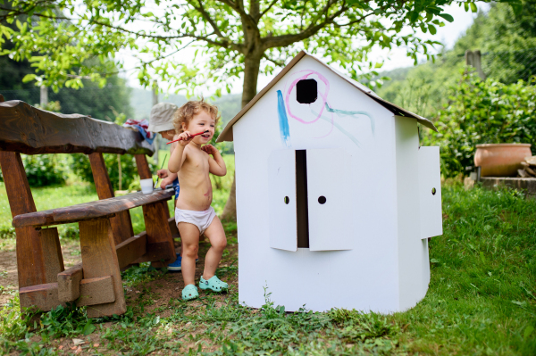 Portrait of topless small blond boy and girl painting outdoors in summer.