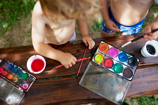 Midsection of unrecognizable boy and girl painting outdoors in summer.