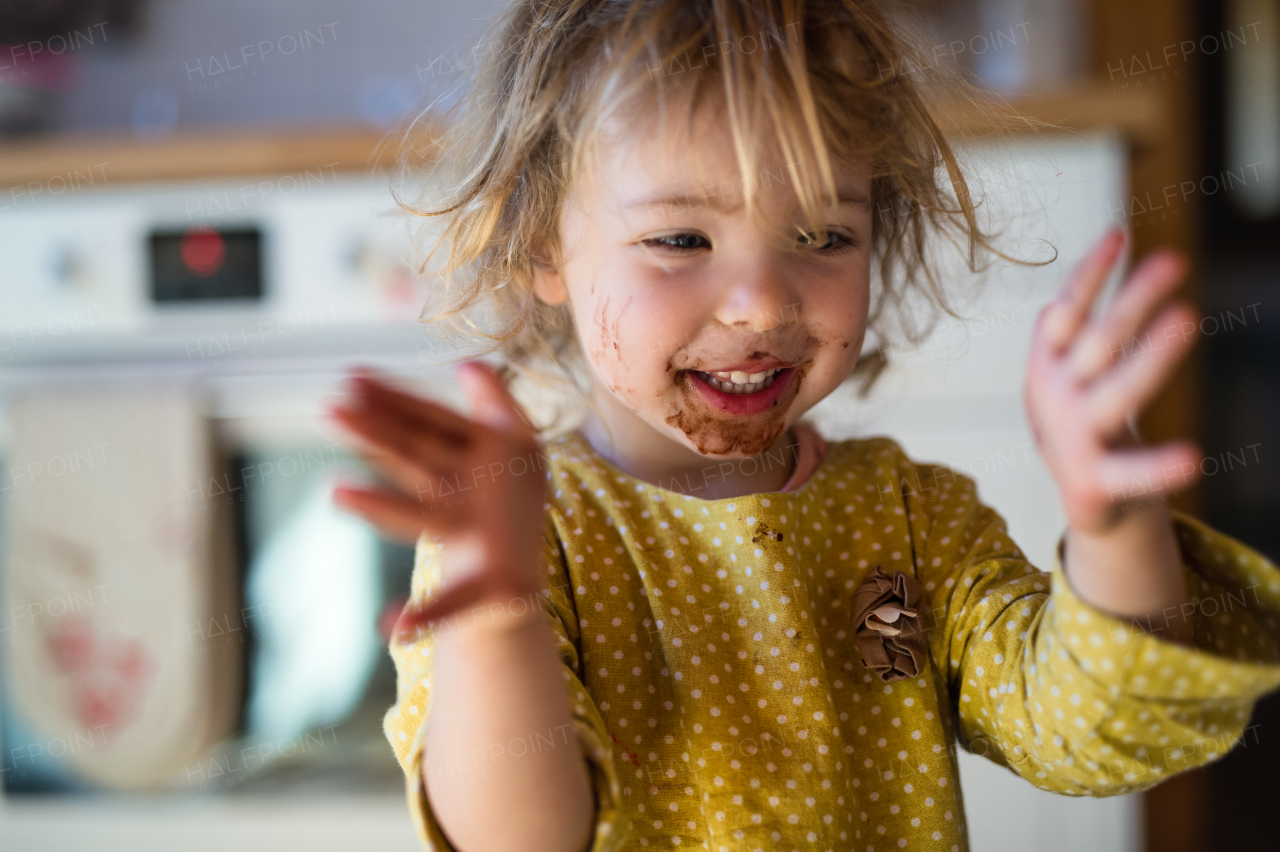 Cheerful small girl with dirty mouth indoors in kitchen at home, clapping.