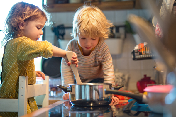 Happy small boy and girl indoors in kitchen at home, helping with cooking.