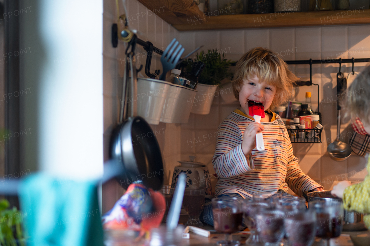 Portrait of happy small boy indoors in kitchen at home, helping with cooking.