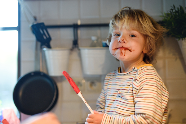 Happy small boy indoors in kitchen at home, helping with cooking.