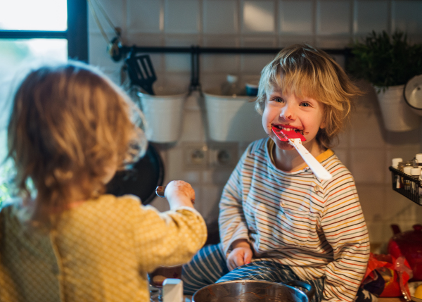 Happy small boy and girl indoors in kitchen at home, helping with cooking.