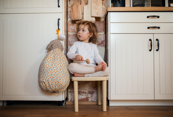 Front view portrait of mall girl sitting indoors in kitchen at home.