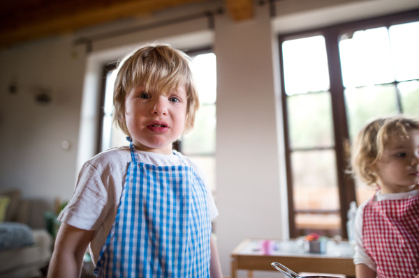 Portrait of unhappy mall boy and girl with apron playing indoors at home.