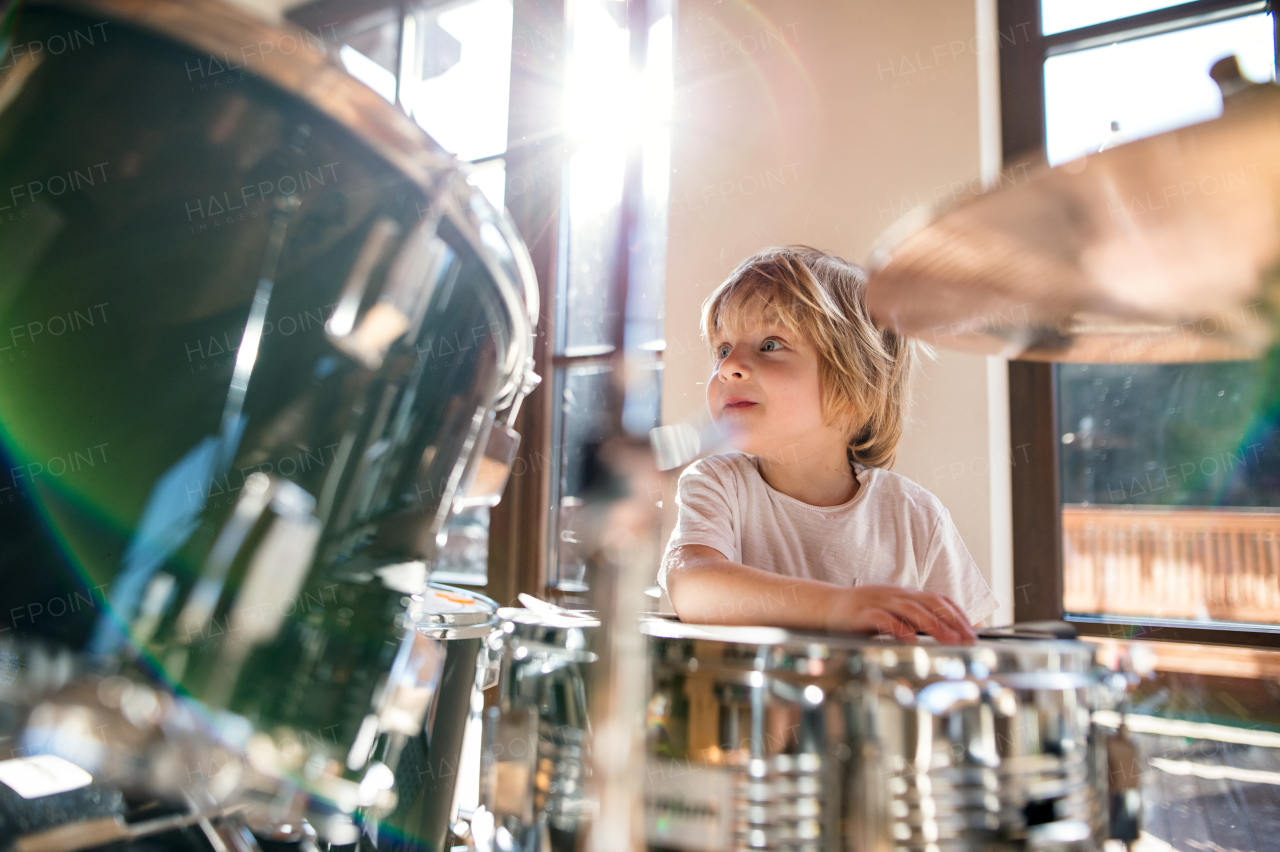 Portrait of happy small boy indoors at home, playing drums.