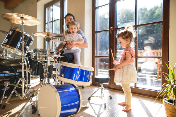 Portrait of happy small children with father indoors at home, playing drums.