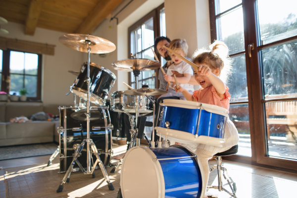 Portrait of happy small girl indoors at home, playing drums.