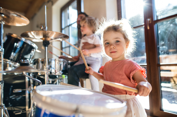 Portrait of happy small girl indoors at home, playing drums.