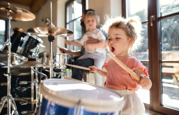 Portrait of happy small girl indoors at home, playing drums.