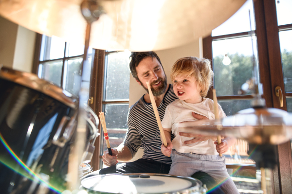 Happy small boy with father indoors at home, playing drums.