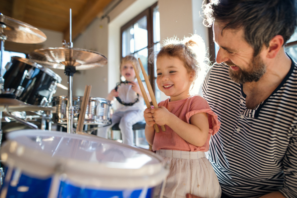 Portrait of happy small children with father indoors at home, playing drums.